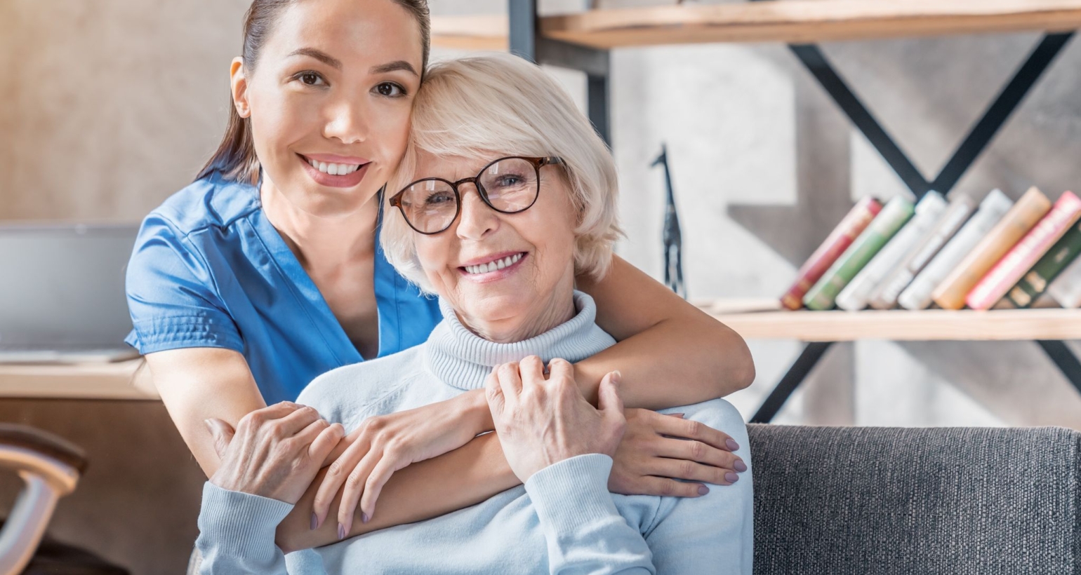 Portrait of female caretaker hugging happy elderly woman indoors