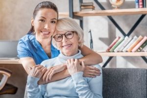 Portrait of female caretaker hugging happy elderly woman indoors